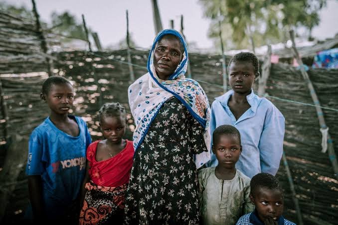 A woman and five children standing outside a woven-branch fence